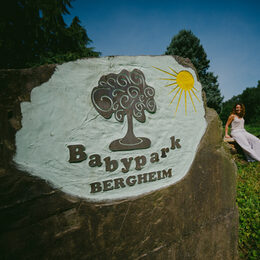 Stein mit Aufschrift "Babypark Bergheim", blauer Himmel, Frau im Hintergrund mit Fahrrad