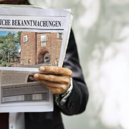 Mann hält Zeitung mit Beschriftung "Öffentliche Bekanntmachungen" und Fotomotiv aus Bergheim auf dem Titel