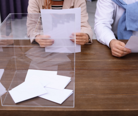 Zwei Menschen an einem Tisch mit einer Wahlurne