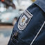 Jacke einer uniformierten Person, Kuli in der Tasche, Wappen und Beschriftung "Ordnungsamt Stadt Bergheim". Hinten unscharf ein Auto