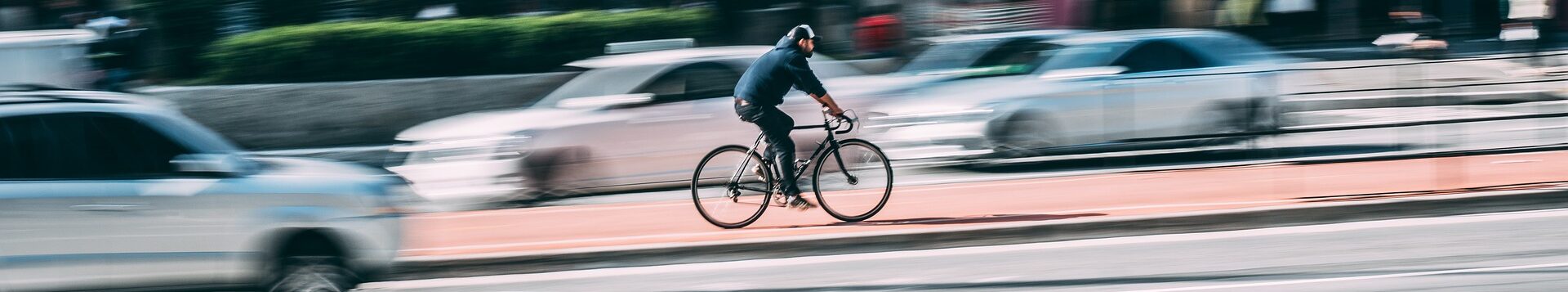 Ein Mensch auf einem Fahrrad fährt mitten auf der Straße entgegen dem Autoverkehr auf einem Radweg. Die Autos sind alle unschraf, der Radfahrer ist im Zentrum des Bildes und scharf