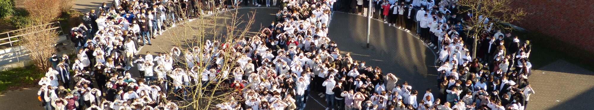 weißgekleidete Schülerinnen und Schüler auf dem Schulhof formieren ein Friedenssymbol