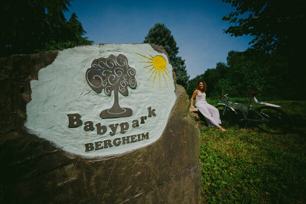 Stein mit Aufschrift "Babypark Bergheim", blauer Himmel, Frau im Hintergrund mit Fahrrad