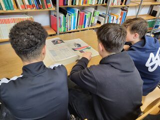 Jugendliche beim Lesen alter Zeitungsbände