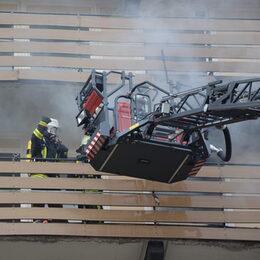 Feuerwehreinsatz mit Tragkorb an Drehleiter, eine Person auf dem Balkon, von dem Rauch herausdringt