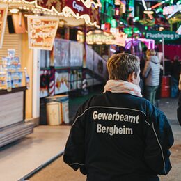 Frau mit Uniform, auf der Rückseite Schriftzug "Gewerbeamt Bergheim" abends auf einer Kirme